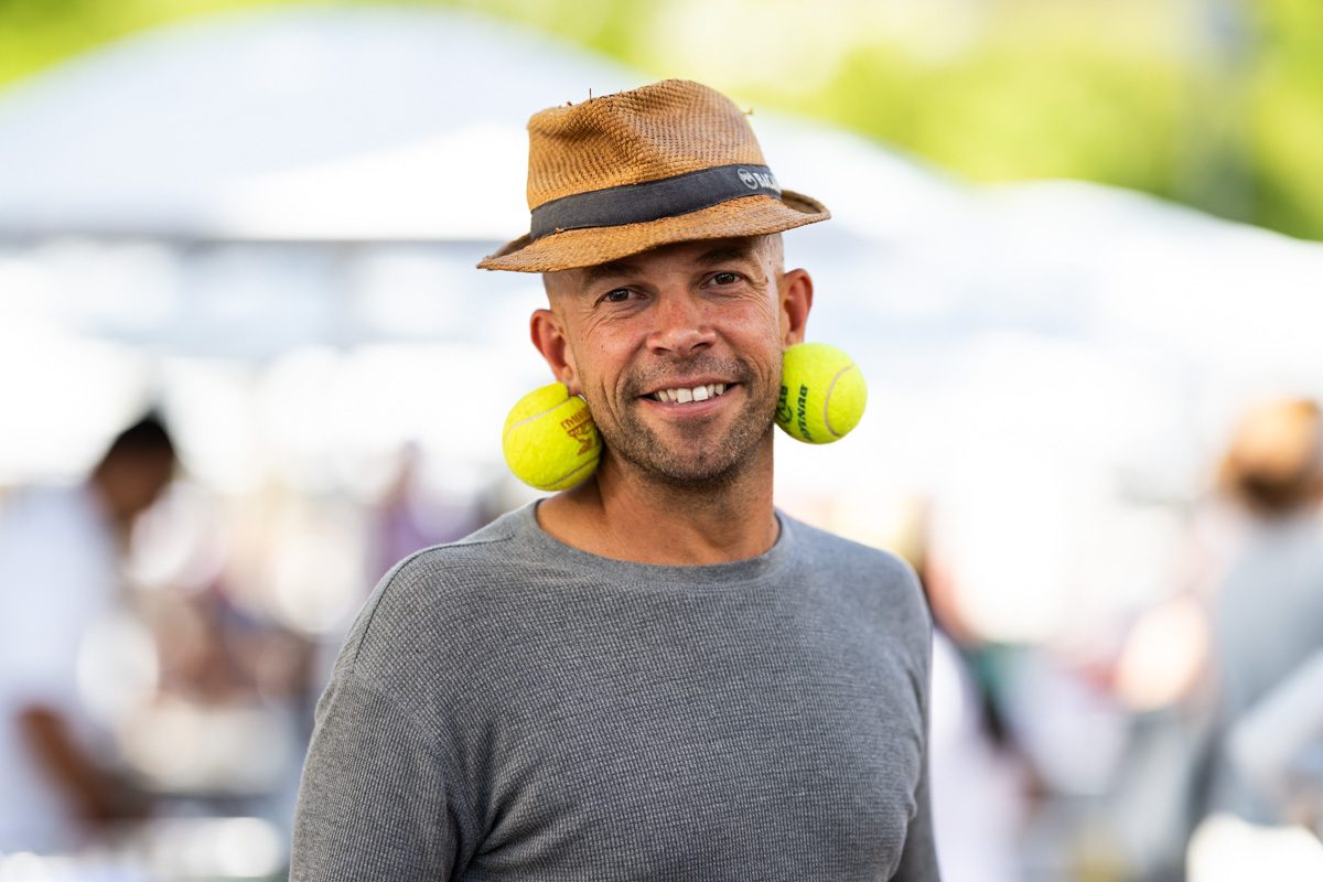 Portrait of a smiling fan with tennis ball earrings and straw hat at the 2025 US Open grounds.