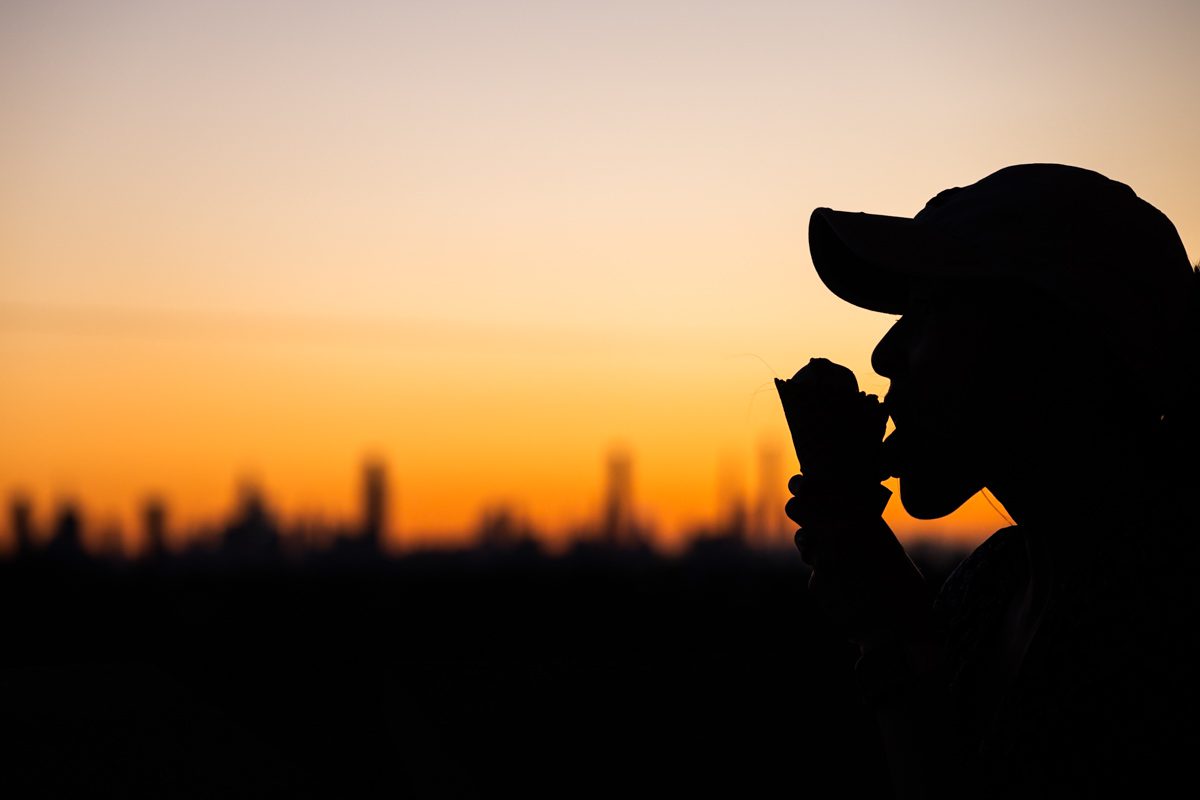 Silhouette of a fan eating ice cream at sunset with NYC skyline glowing in background during 2025 US Open.