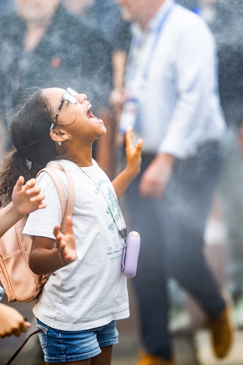 Young fan enjoying the mist cooling station at the 2025 US Open, arms raised in joy.