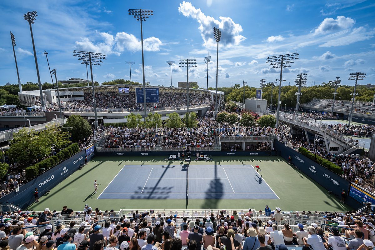 Wide view of Grandstand packed with fans at the 2025 US Open, bright blue skies above the court.