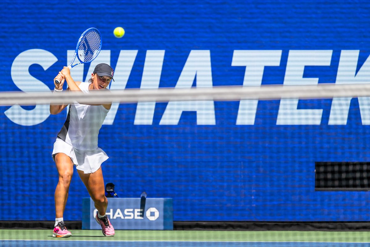 Iga Świątek hitting a clean backhand in front of her name signage at the 2025 US Open.