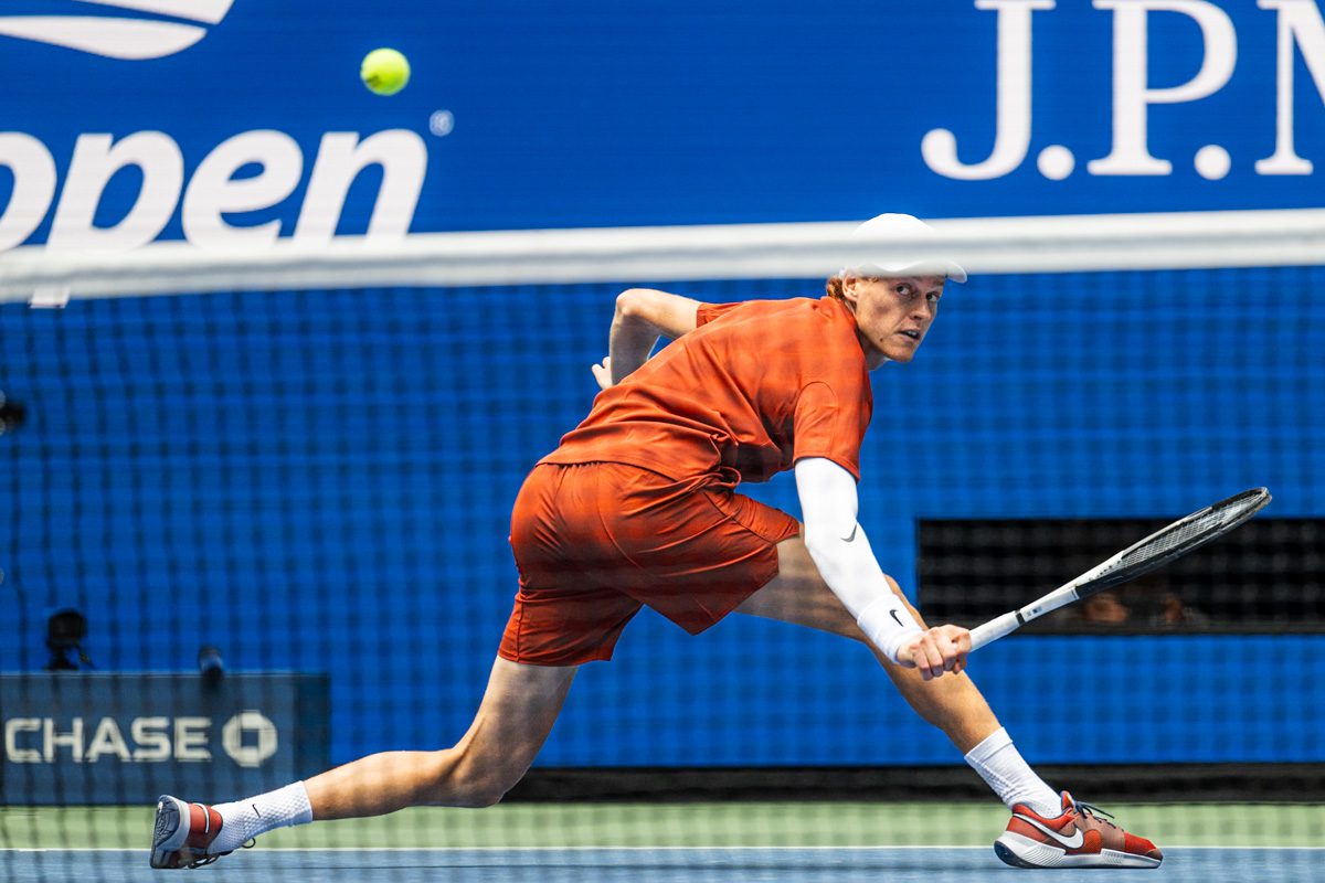 Jannik Sinner stretched low for a backhand on hardcourt at the 2025 US Open, eyes locked on the ball.