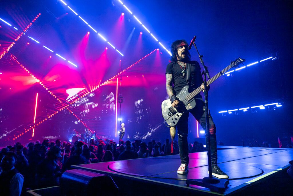 The band’s bassist performs on the runway under bold red and blue LED truss lighting, captured up close to emphasize color and structure.