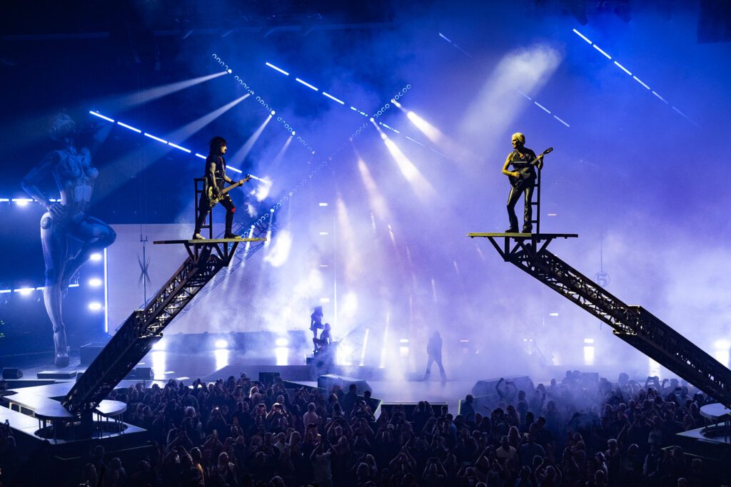 Two Mötley Crüe band members elevated on risers surrounded by blue haze and beams, highlighting PRG’s large-scale stage design and motion.