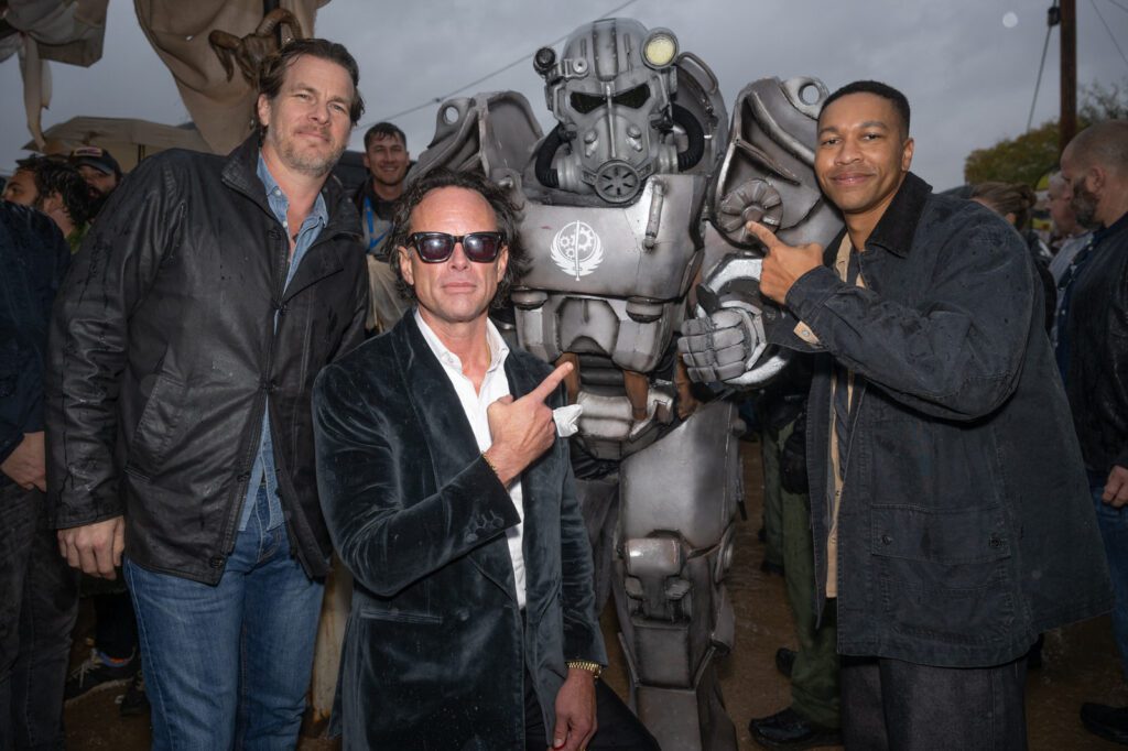Three men pose with a fan dressed in a power-armor suit during the outdoor Fallout celebration.