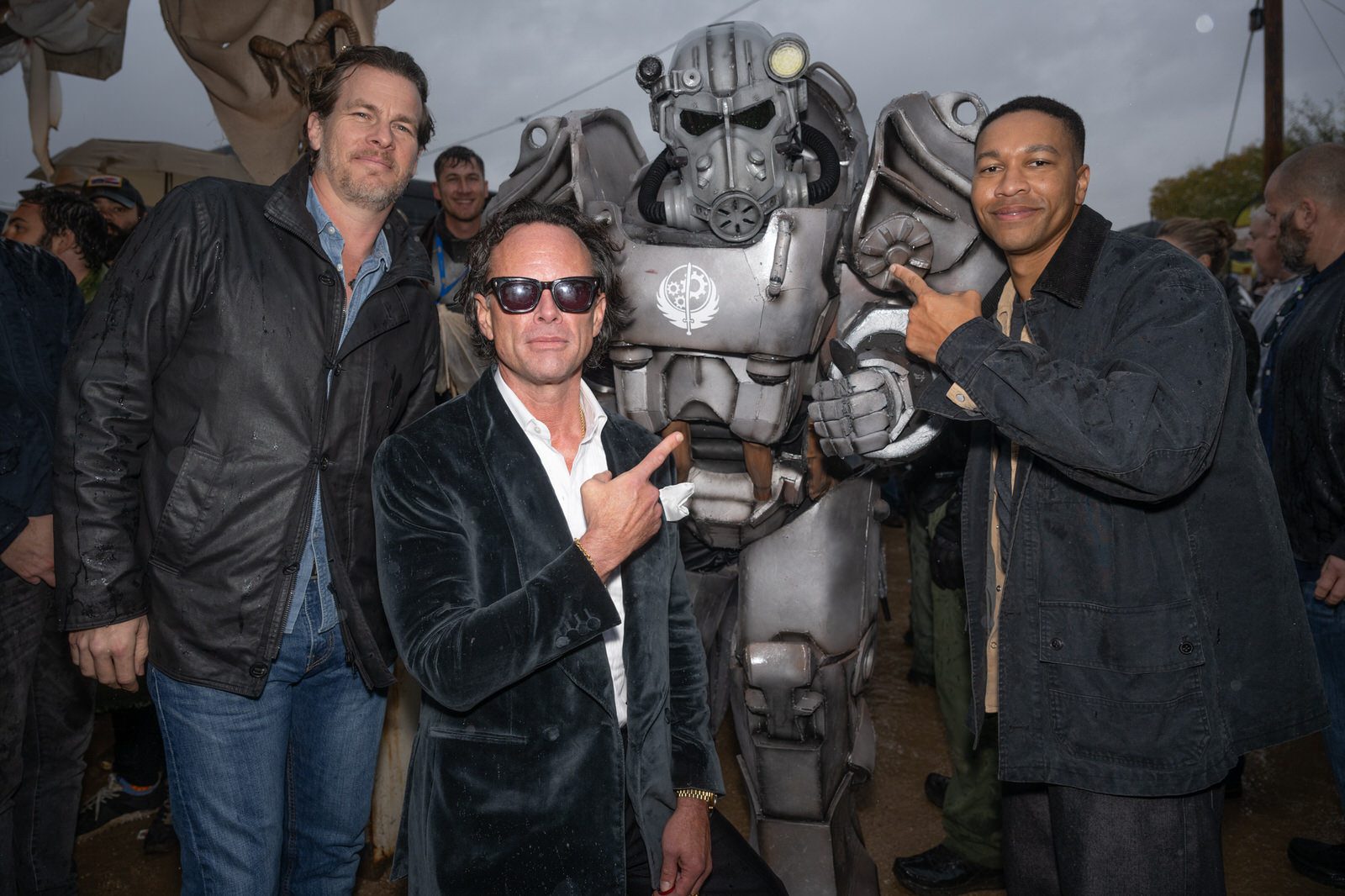 Three men pose with a fan dressed in a power-armor suit during the outdoor Fallout celebration.
