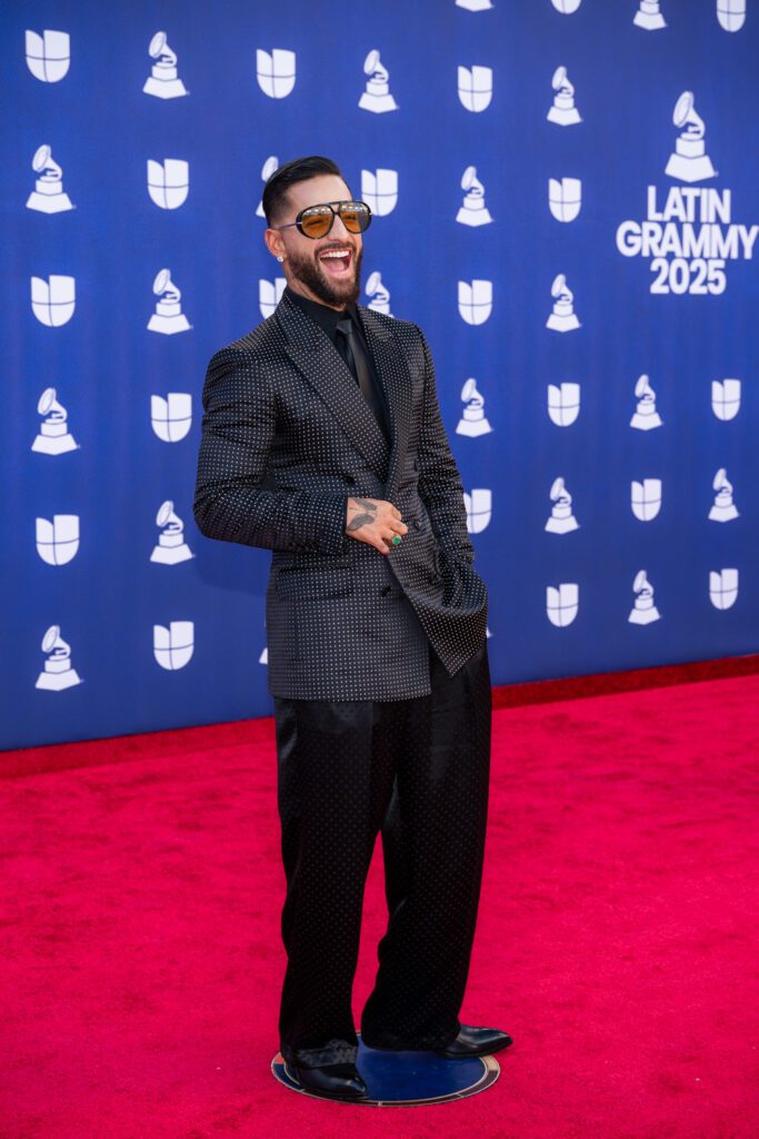 Maluma smiles while posing on the Latin Grammy red carpet in a dark patterned suit.