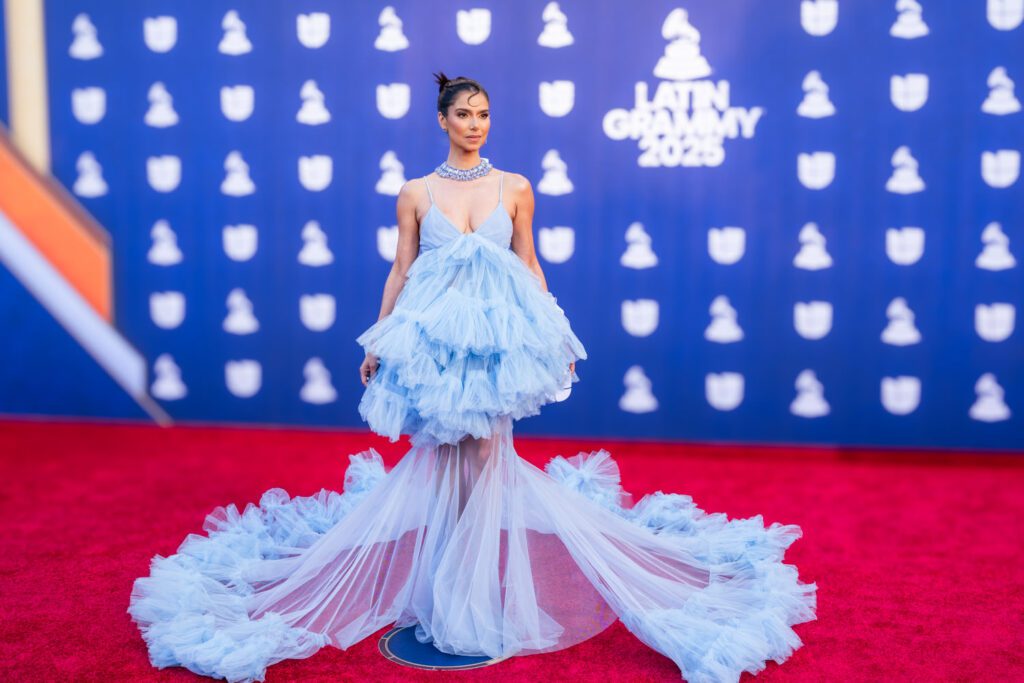 Roselyn Sanchez poses on the Latin Grammy red carpet wearing a dramatic light-blue tiered gown with a long flowing train.