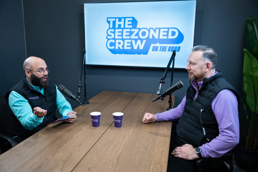 Two people recording The Seezoned Crew On The Road podcast inside the Pinewood.AI booth at NADA 2026 in Las Vegas